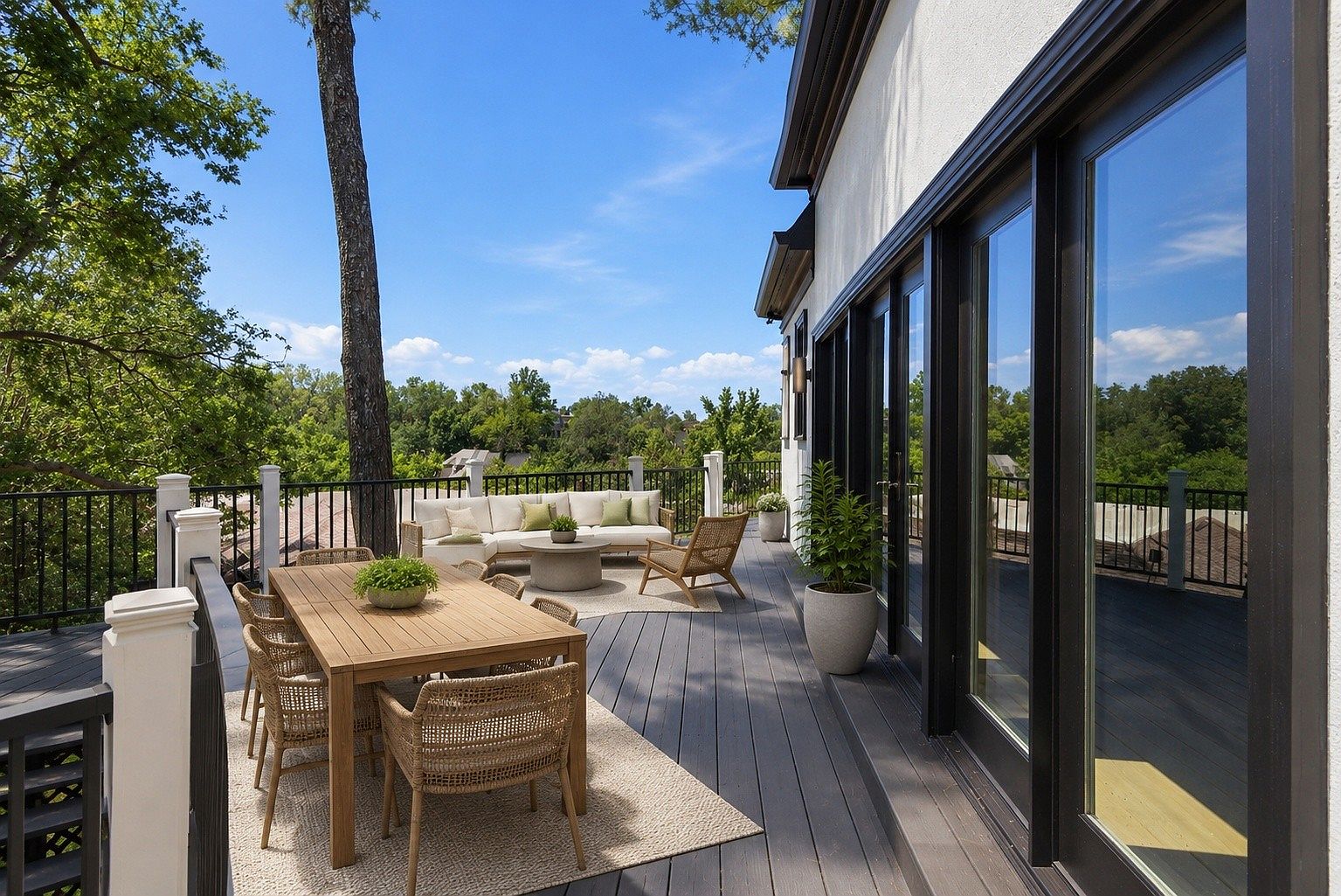 Wide view of the rear deck at 105 Burlington Ct with a teak dining table, wicker chairs, a lounge grouping, and treetops rolling out to the horizon