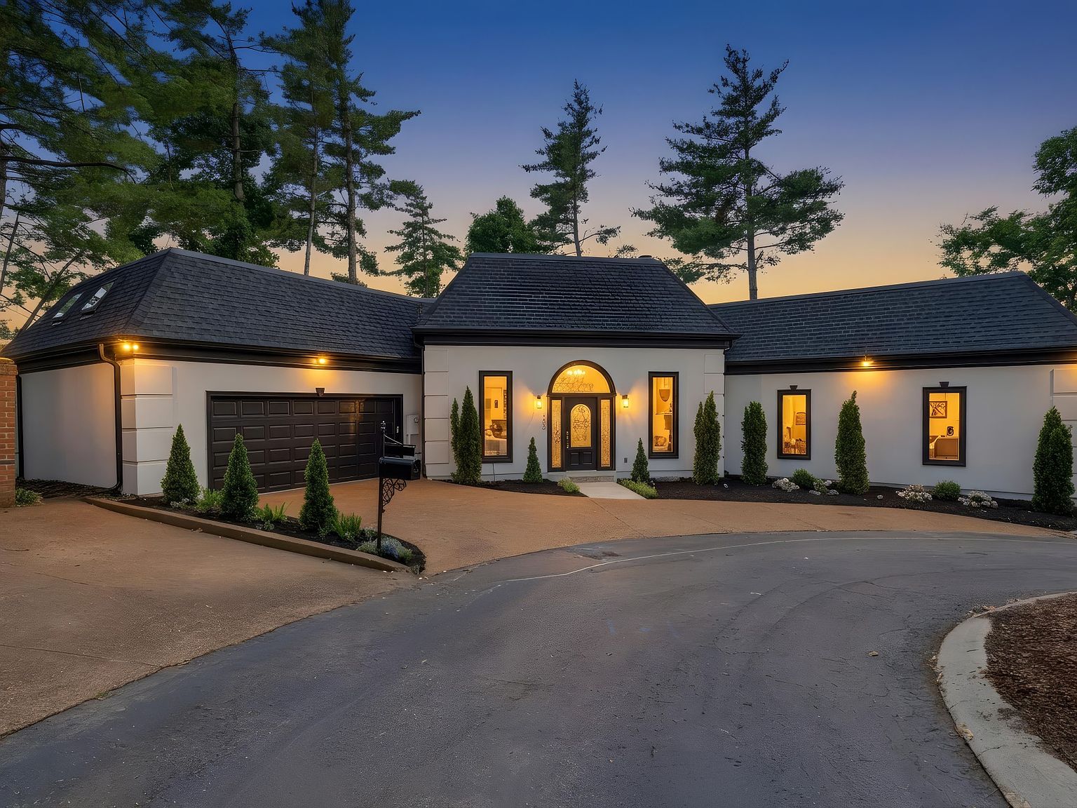 Twilight facade of 105 Burlington Ct, a remodeled white one-story home with a slate roof, arched entryway, and warm interior lights, held above the cul-de-sac by mature Tennessee evergreens